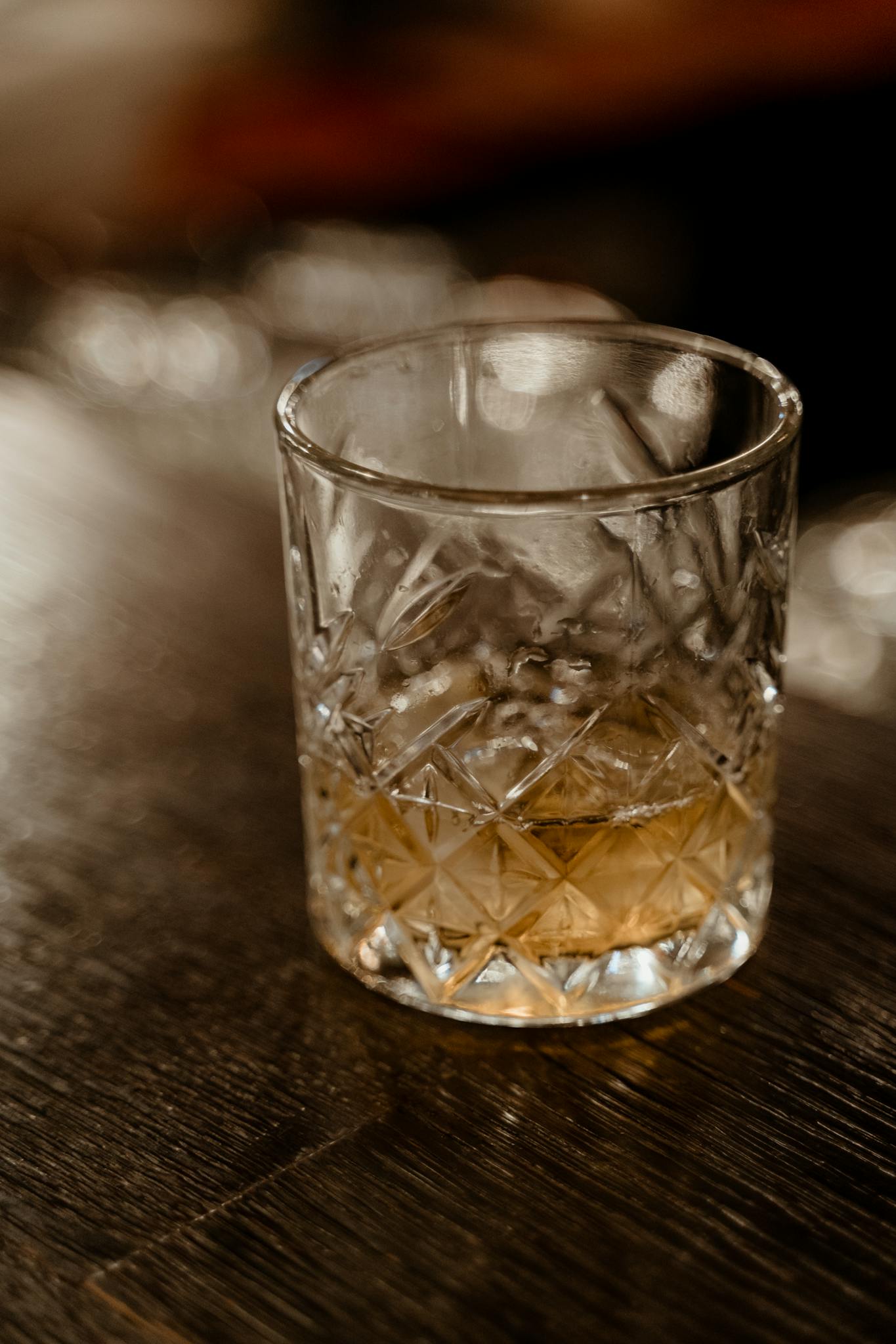 A close-up shot of whiskey served in a patterned crystal glass on a wooden surface.