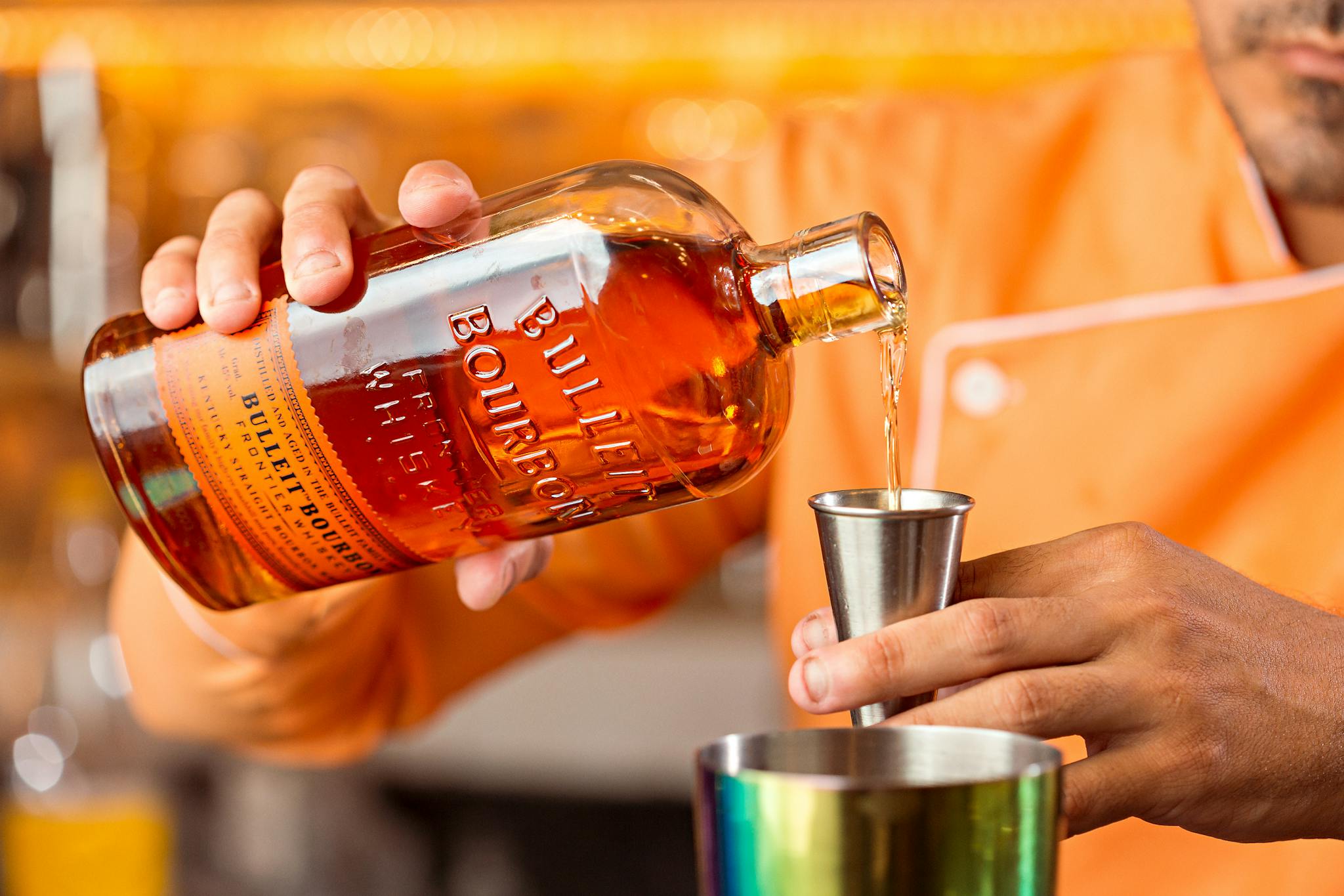 Close-up of bartender pouring bourbon into a jigger for cocktail preparation.